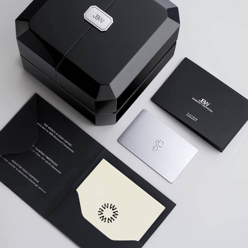 Sleek black gift box with silver Olympia PS | PS510A logo, silver card, black envelope holding a cream card, and branded black booklet by JBW—perfect for presenting an 18K gold-plated or diamond watch.