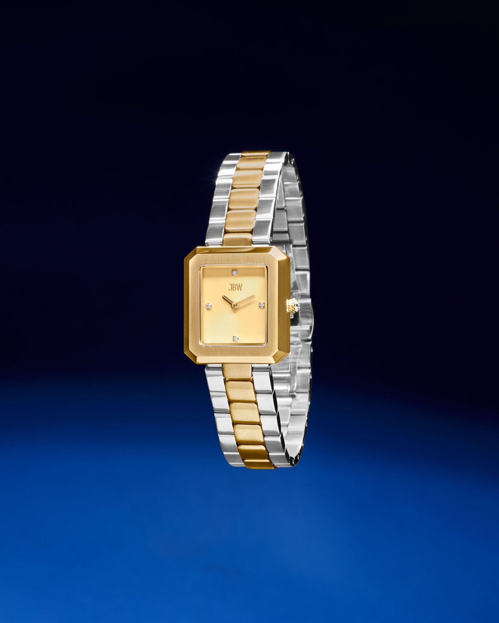 The JBW Watches Arc Single | J6390F is a square-faced, gender-neutral watch with a gold dial and bezel, plus a two-tone strap of gold and silver links, showcased on a dark blue gradient background.