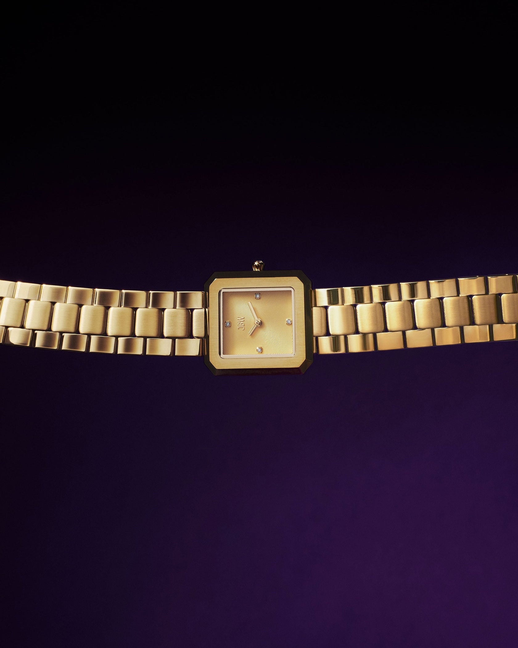 The JBW Watches Arc Single | J6390E is a gold wristwatch featuring a square face and gold metal link band, showcased against a dark purple background.