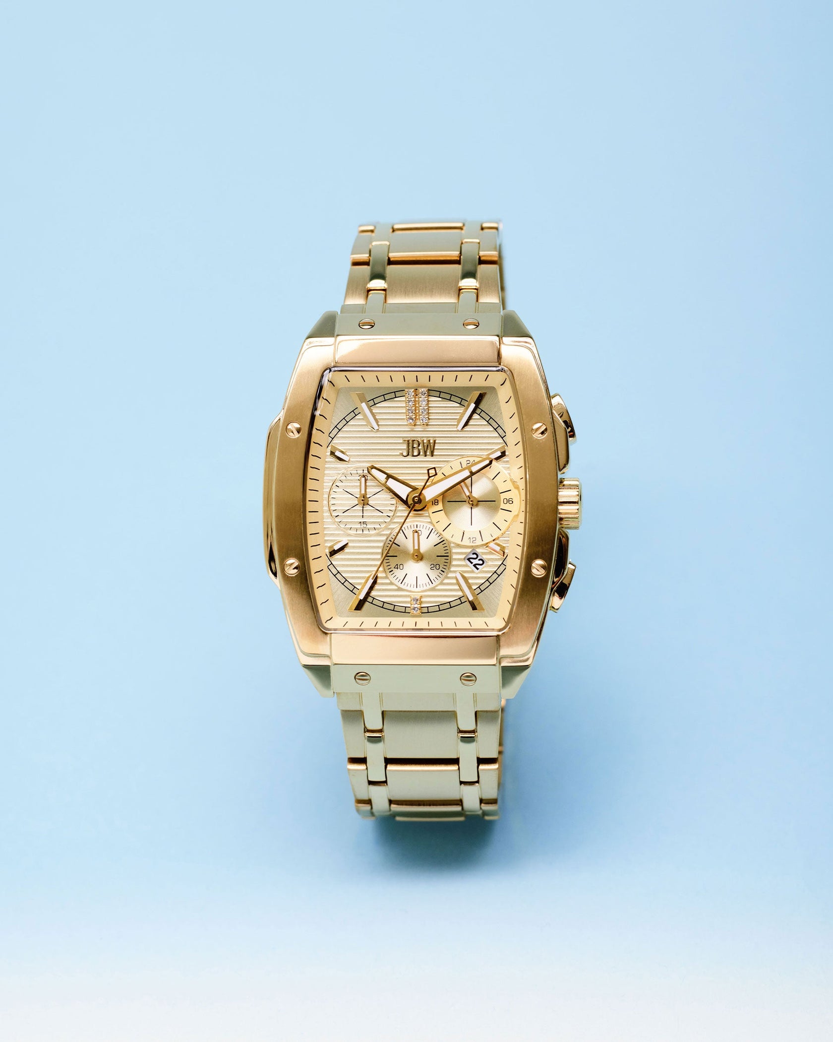 The JBW Watches Echelon | J6409A, an 18K gold-plated rectangular watch with a stainless steel band, textured face, and multiple dials, is displayed on a light blue gradient background.
