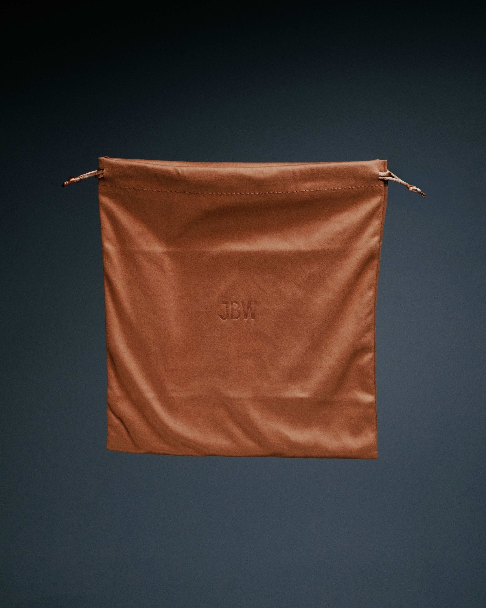 A brown JBW Gift Bag with a drawstring, featuring the JBW logo embossed in the center, is shown against a dark background.