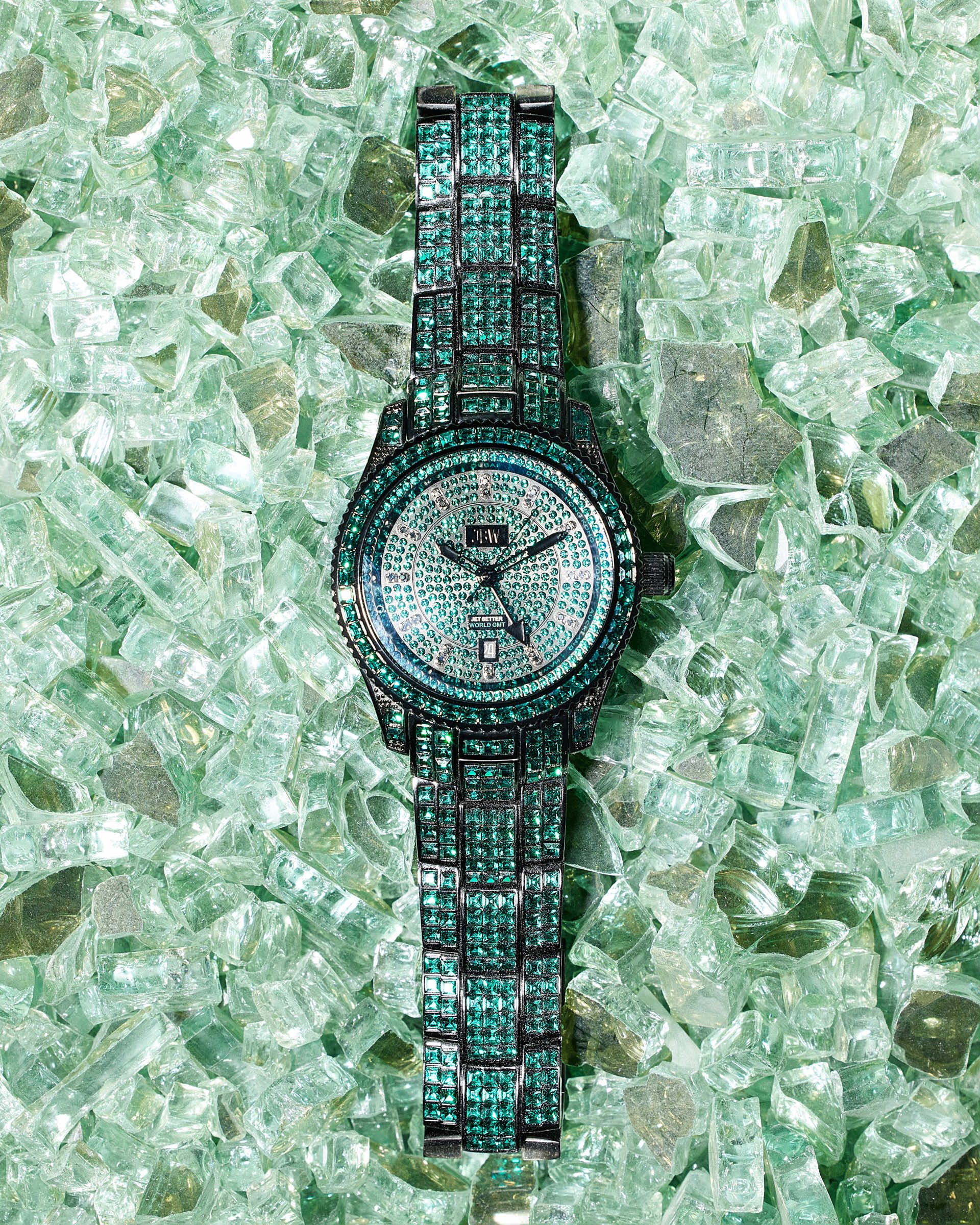 The JBW Watches RESERVE Jet Setter GMT Emerald | R6393C sparkles with green and black gemstones atop shattered green glass, highlighting its luxury design and premium Swiss GMT movement.