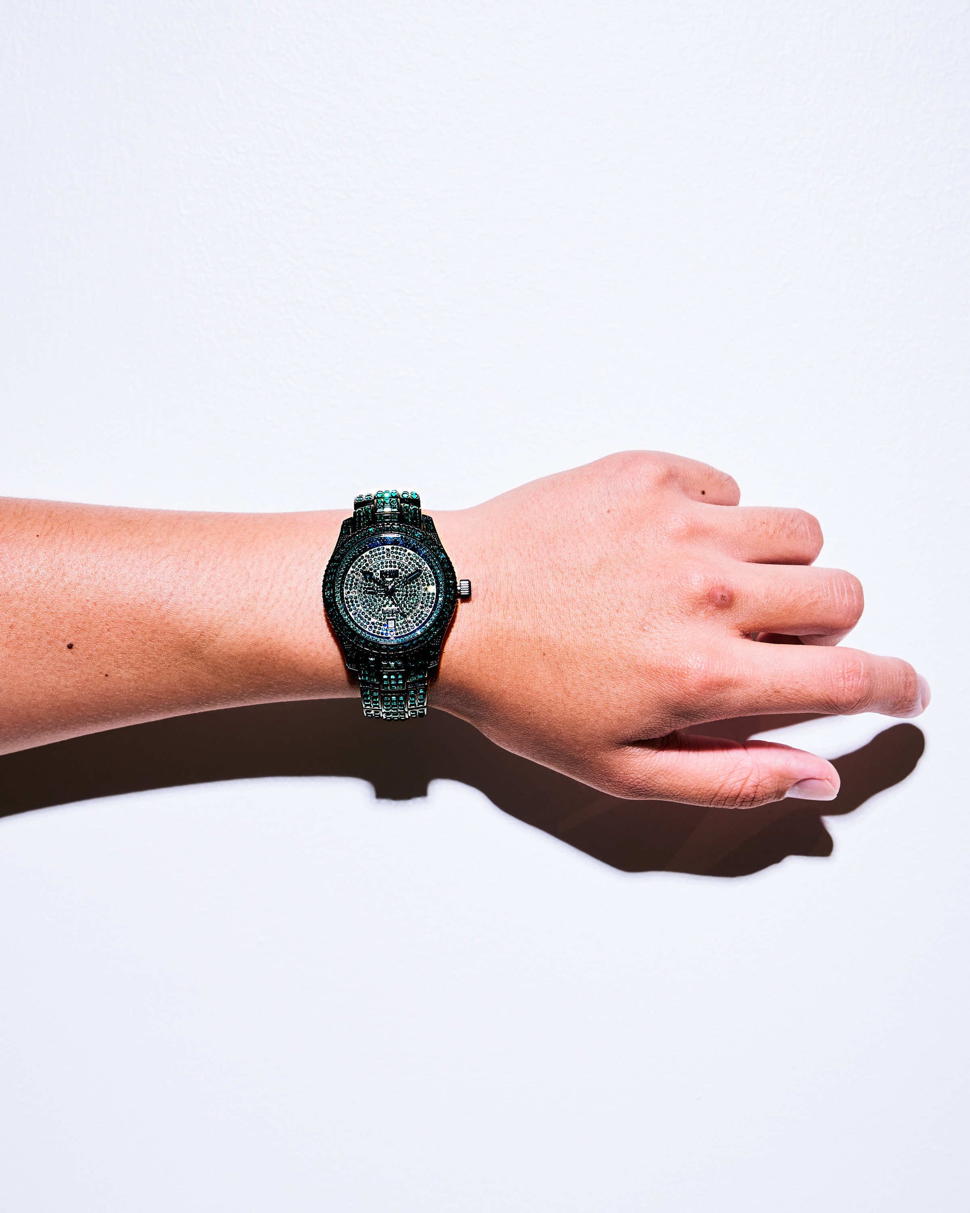 A person’s left wrist wears the JBW Watches RESERVE Jet Setter GMT Emerald | R6393C, a sparkling dark green diamond watch with textured band and Swiss GMT movement, shown against a plain white background.