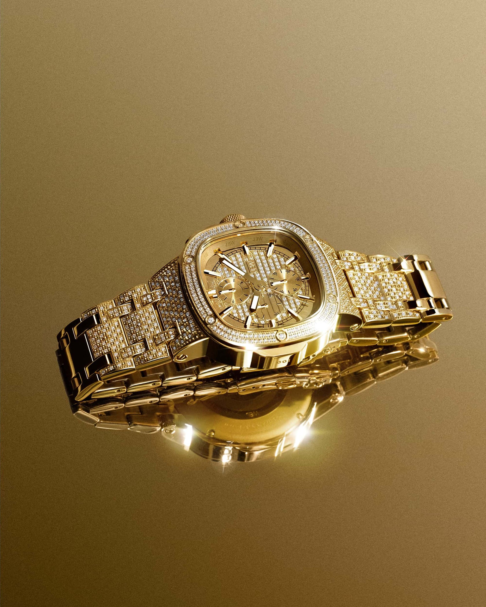 The JBW Watches Heist PS | PS545A features gold-plated stainless steel with a diamond-encrusted bezel and bracelet, displayed on a reflective gold surface for an elegant, opulent look.