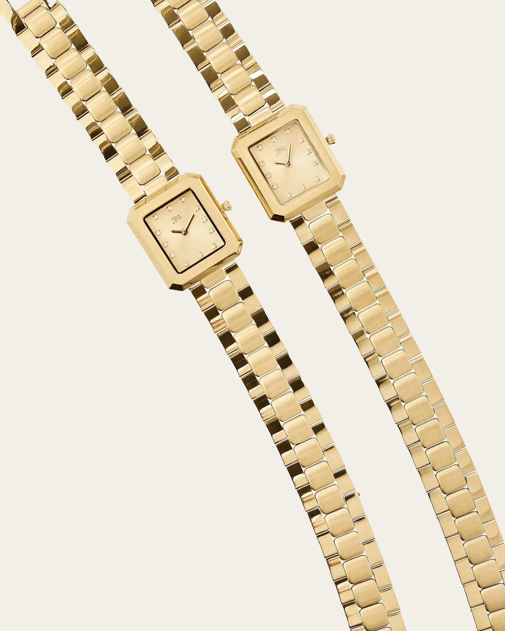 The Arc Double | J6390H by JBW Watches features two gold, gender-neutral, square-faced watches with linked metal bands and minimalist dials marked by small dots, displayed side by side on a light background.