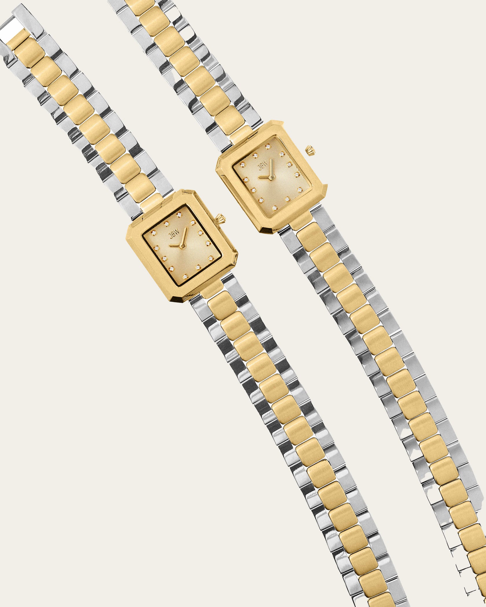 The JBW Watches Arc Double | J6390K features two sleek, gender-neutral watches with rectangular gold faces and silver-gold link bands, displayed side by side. Minimalistic dials with dot hour markers add to their timeless elegance.