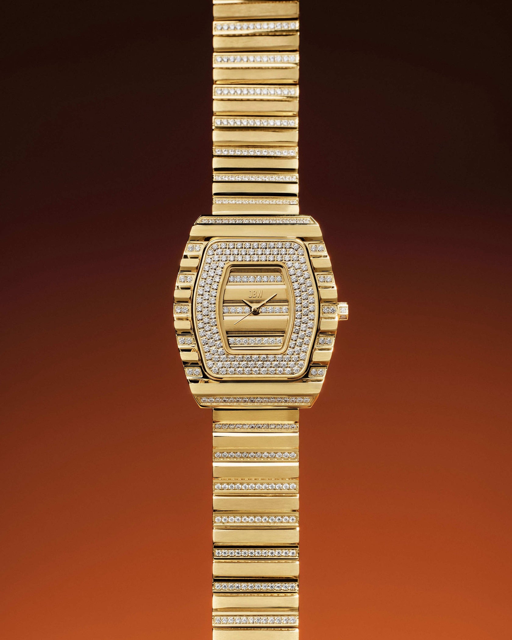 The Atlas | J6404A by JBW Watches is a luxurious gold wristwatch with a rectangular face and band, both adorned with premium crystals and finished in 18k gold-plating, set against a gradient brown-to-orange background.