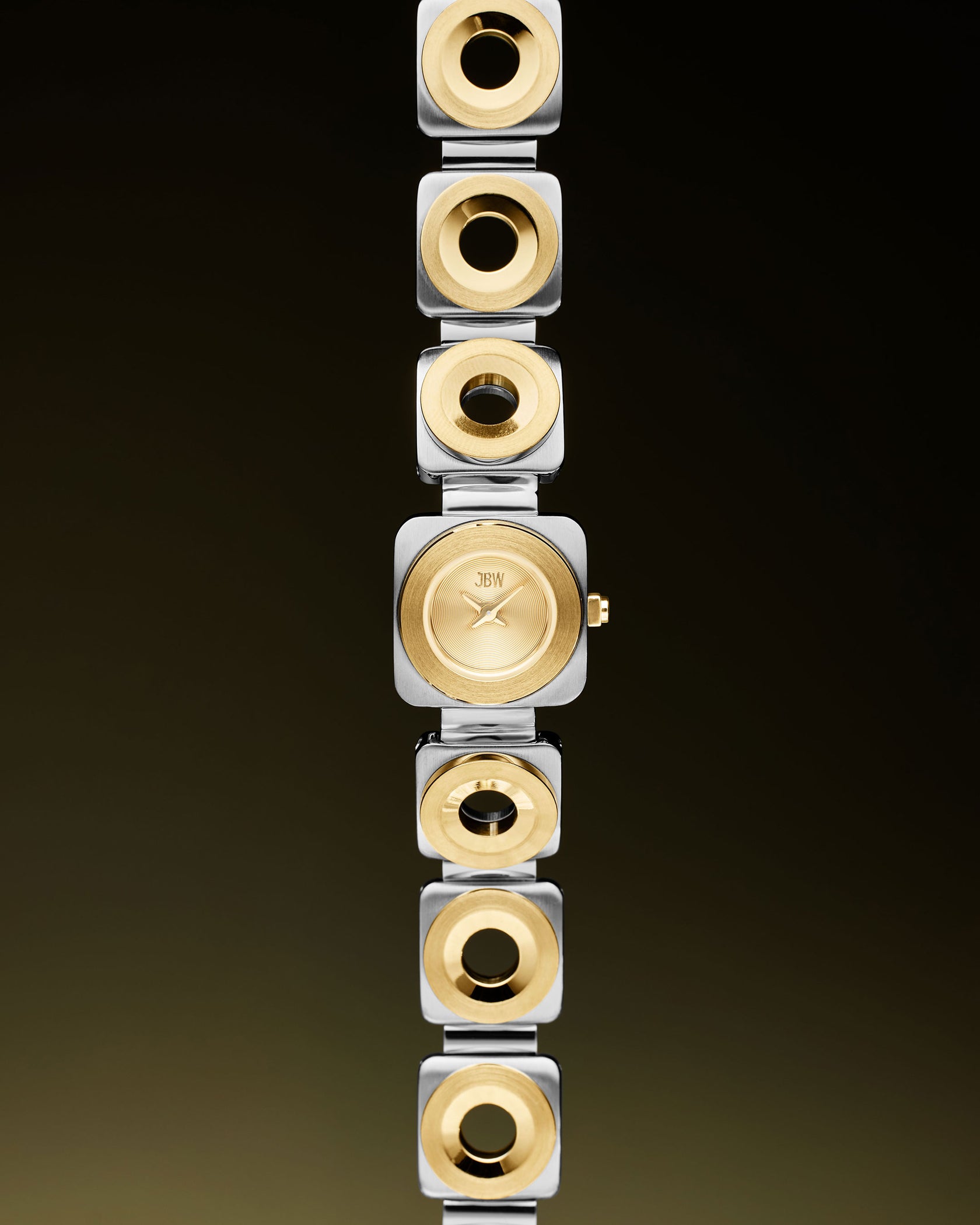 The JBW Watches Chasm Petite | J6400C is an 18k gold-plated watch with a square face and two-tone stainless steel links in silver and gold, set against a dark gradient background.