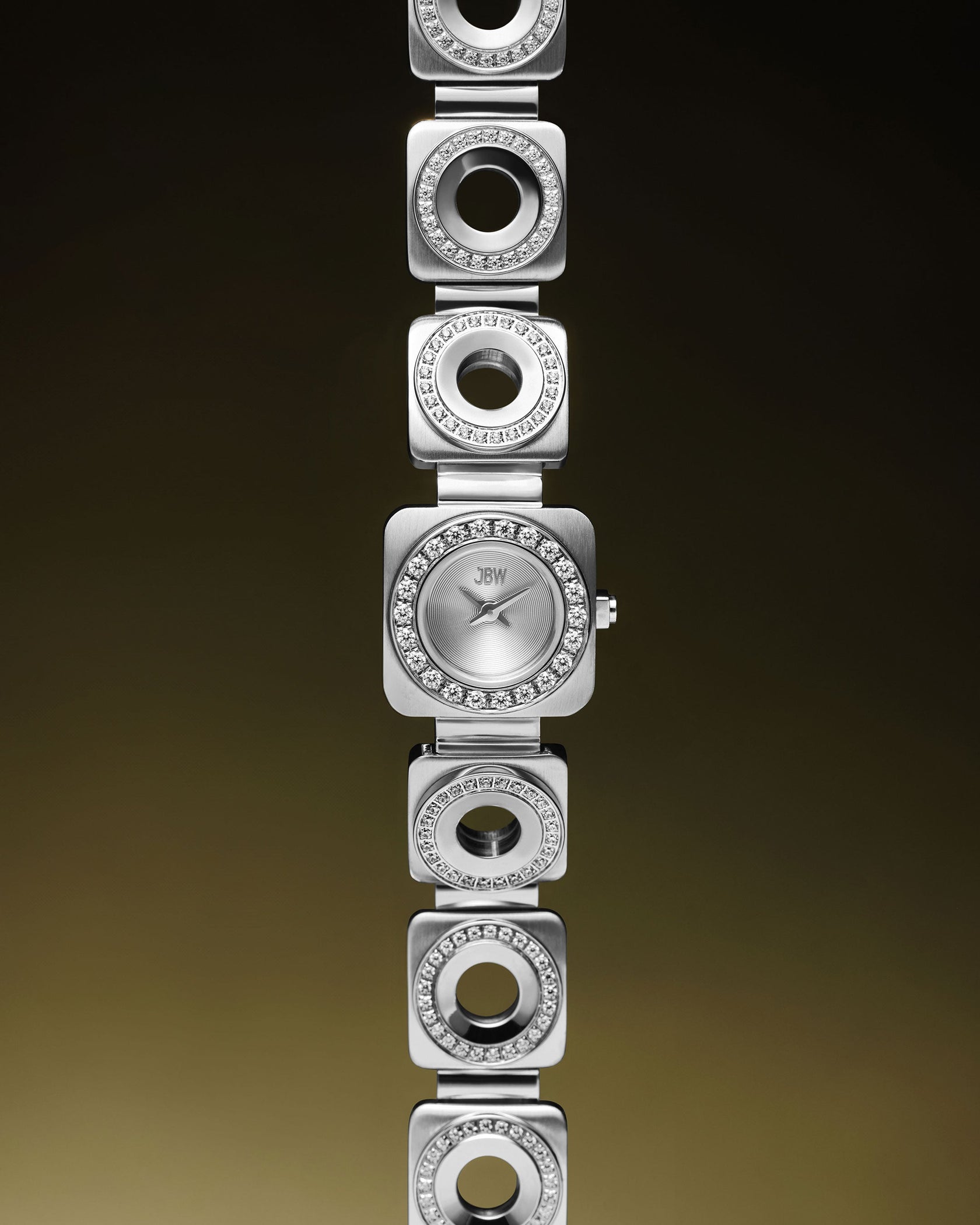 The JBW Watches Chasm | J6399B is a stainless steel watch with a square face and diamond accents on the dial and circular links, featuring Swiss Ronda 751 movement, displayed vertically on a gradient brown background.