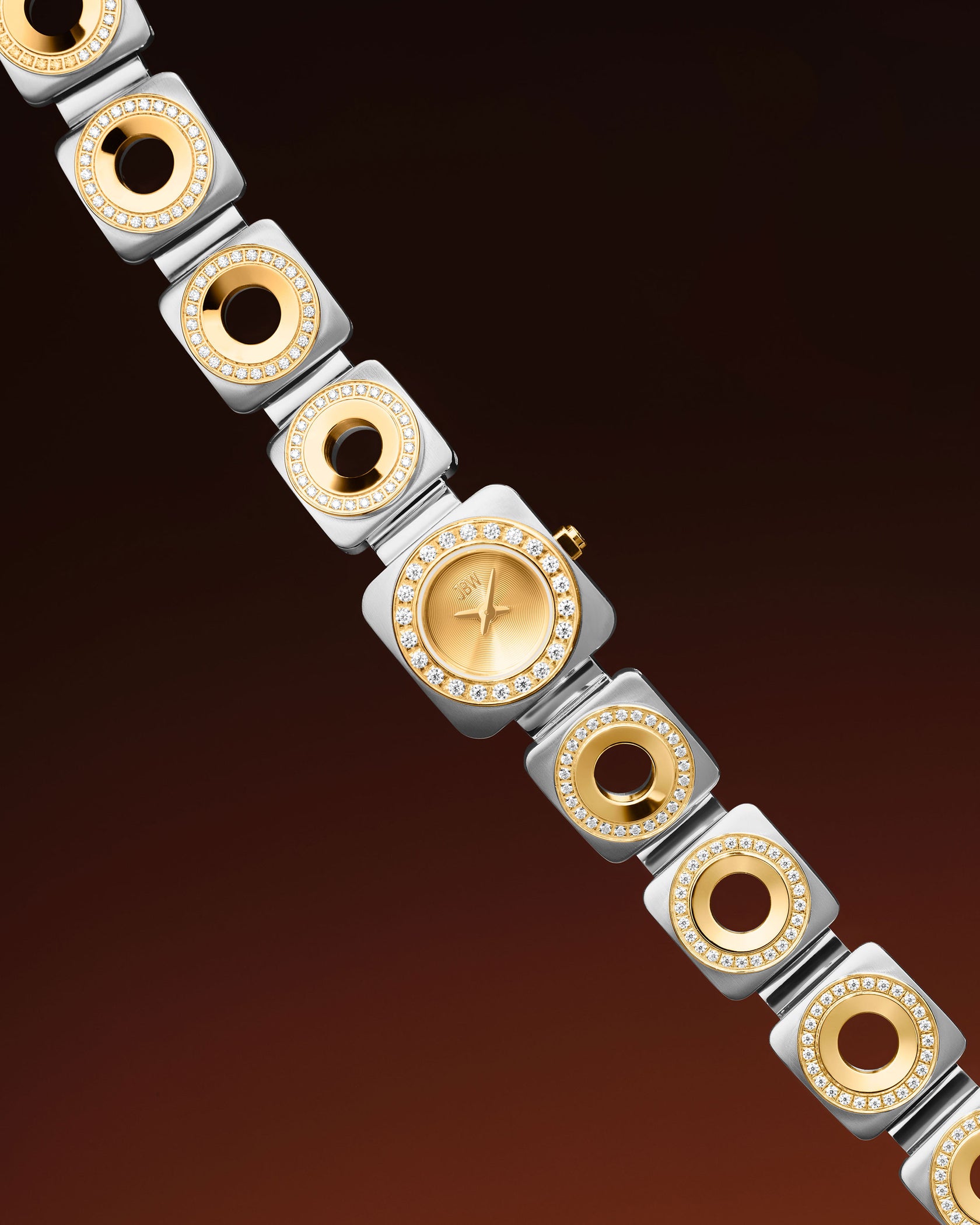 The Chasm Petite | J6401C by JBW Watches is an 18k gold-plated watch with a gold and silver square-link band, premium crystals on each link, and a gold face, shown diagonally on a dark brown gradient background.