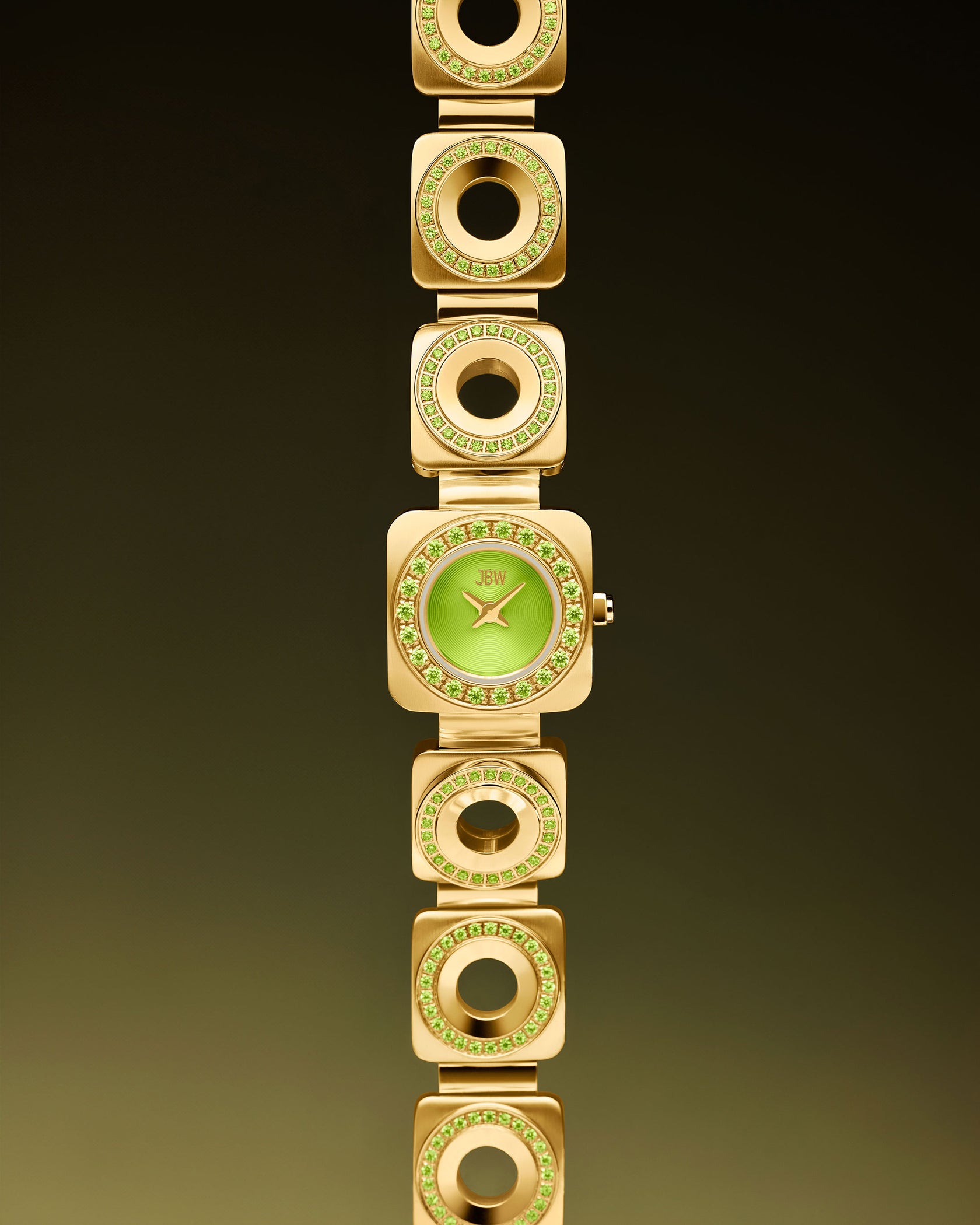Introducing the Chasm Petite | J6401D by JBW Watches: an 18k gold-plated watch with a green face, gold hands, and square gold links with circular cutouts accented by premium crystals—elegantly showcased on a dark gradient backdrop.