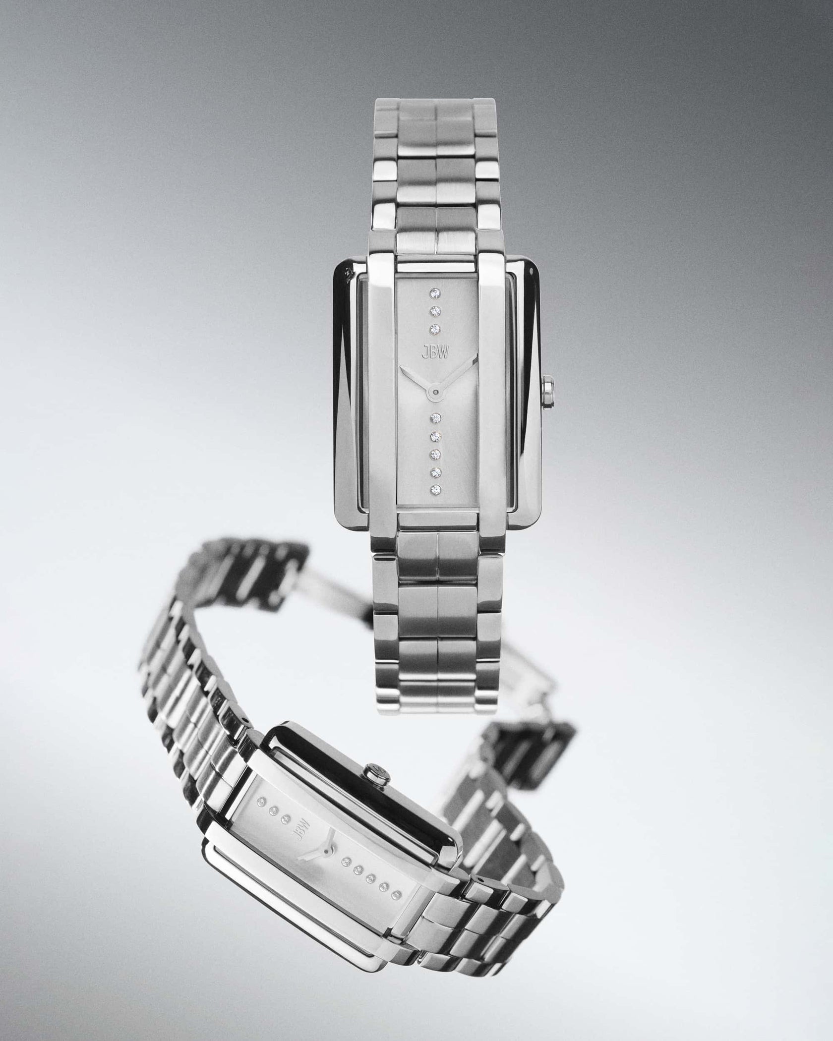 Two sleek, rectangular silver JBW Watches Mink Petite | J6395B timepieces with metal link bands are shown. Their minimalist faces feature lab grown diamonds as raised dots; one watch stands upright and the other is angled.