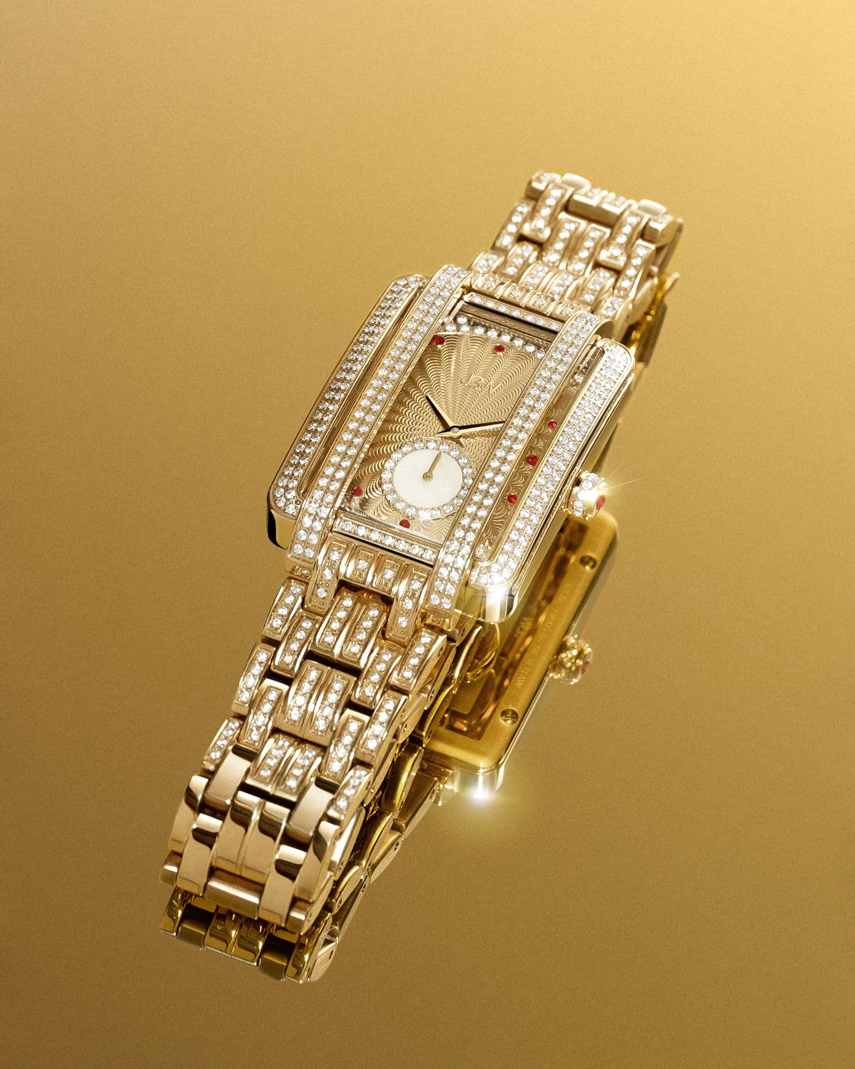 The JBW Watches Mink PS | PS505A features a luxurious 18K gold-plated rectangular case, adorned with diamonds and rubies, displayed on a reflective gold surface to highlight its detailed face and bracelet.