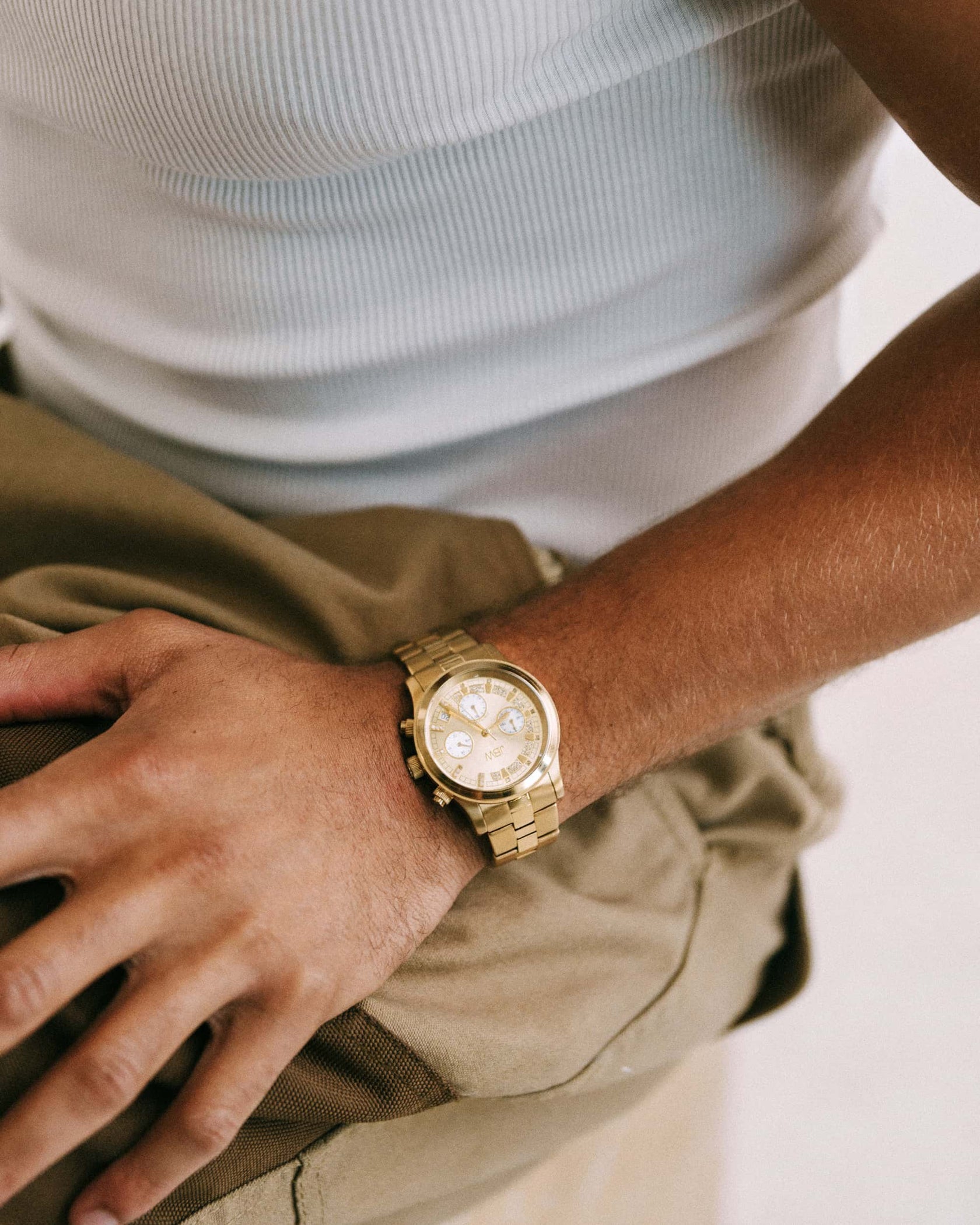 Wearing the JBW Muse | JB-6217-E 18K gold-plated watch and a white ribbed tank top, a person rests their hand on a khaki-colored bag.