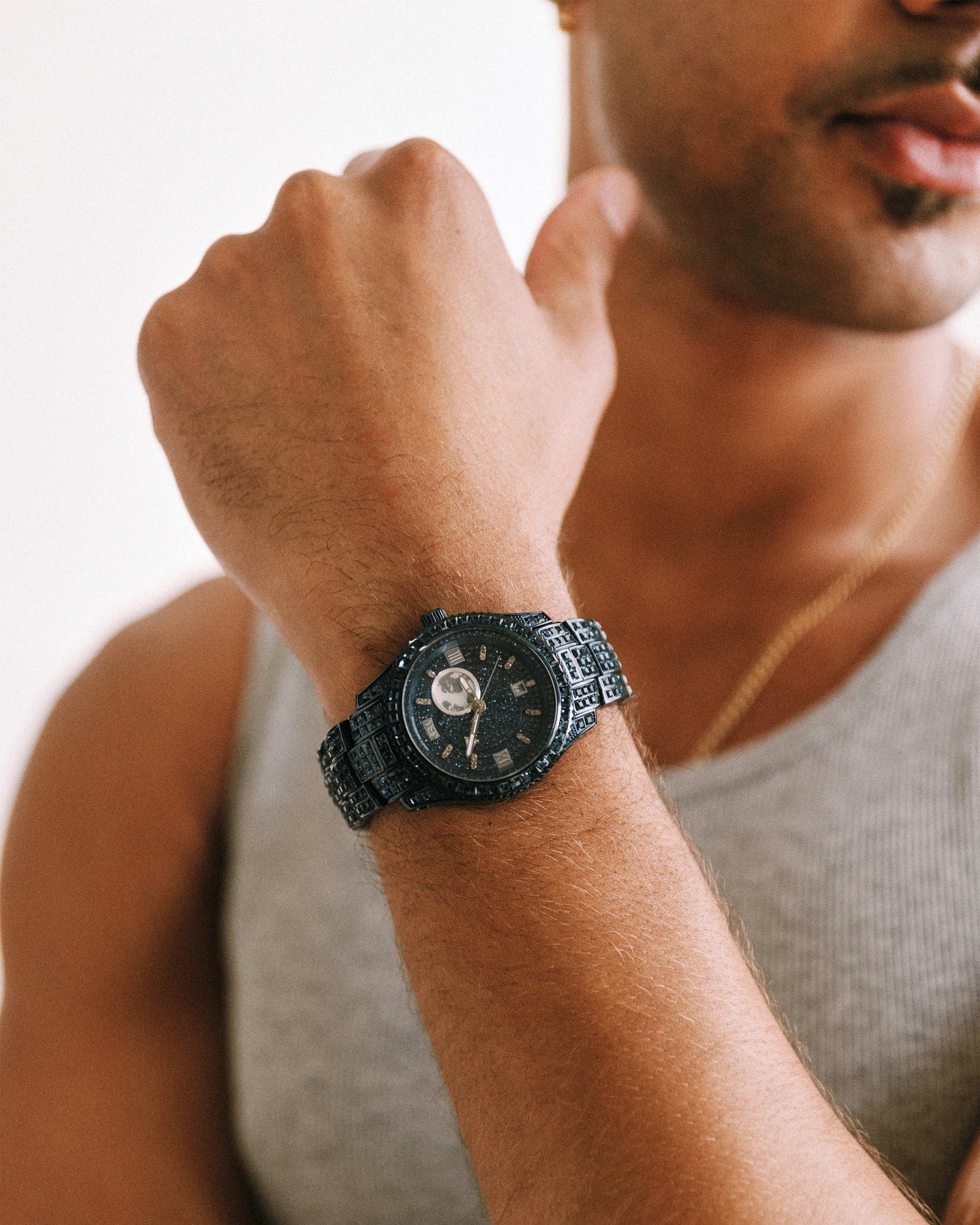 A person wearing a gray tank top displays the JBW Watches RESERVE Bleu 39 | R6393A-GA (Grade A) wristwatch on their left wrist, arm bent and fist raised near their face.