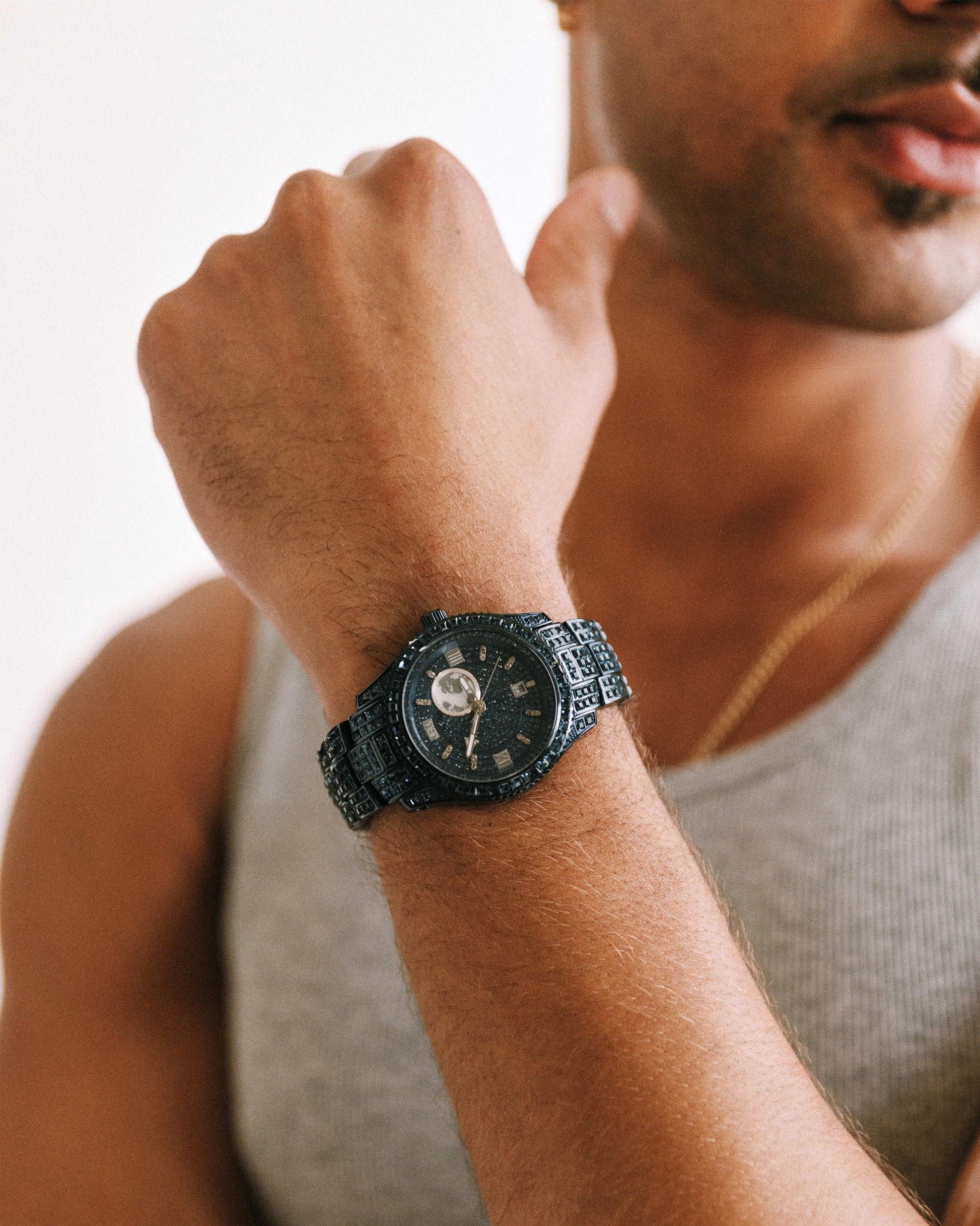 A person wearing a gray tank top displays the JBW Watches RESERVE Bleu 39 | R6393A-GA (Grade A) wristwatch on their left wrist, arm bent and fist raised near their face.