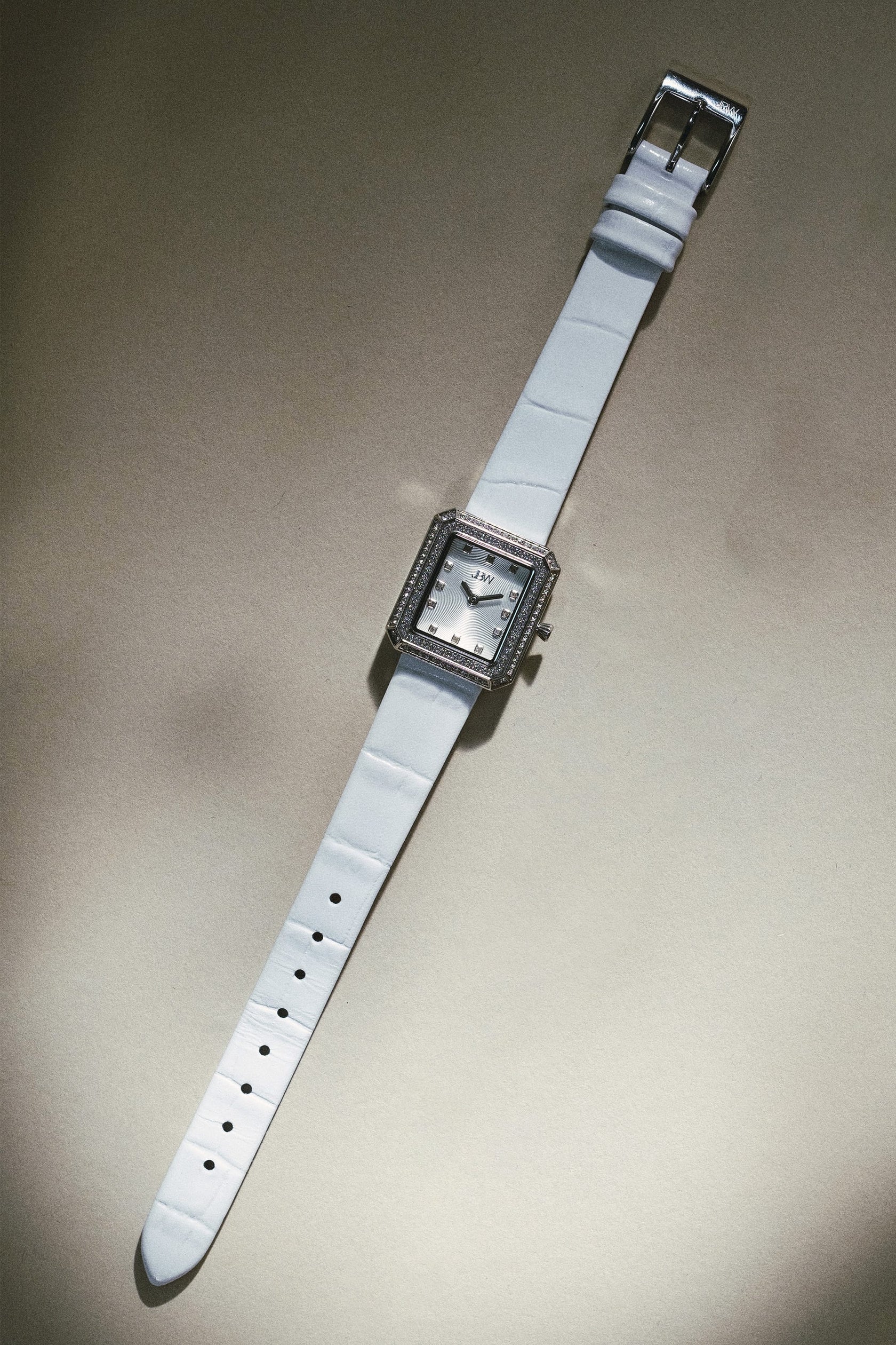 The JBW Watches Arc Leather | J6390LC, a silver square-faced unisex watch with a white leather band and rhinestones around the dial, is displayed on a neutral background.
