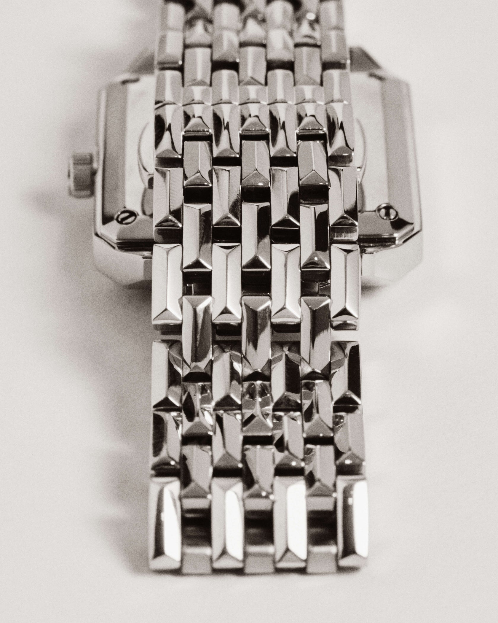 A close-up black-and-white photo of the JBW Watches Astra | J6411A, featuring a metallic square silhouette, rectangular face, and shiny geometric metal link bracelet, taken from the strap side.