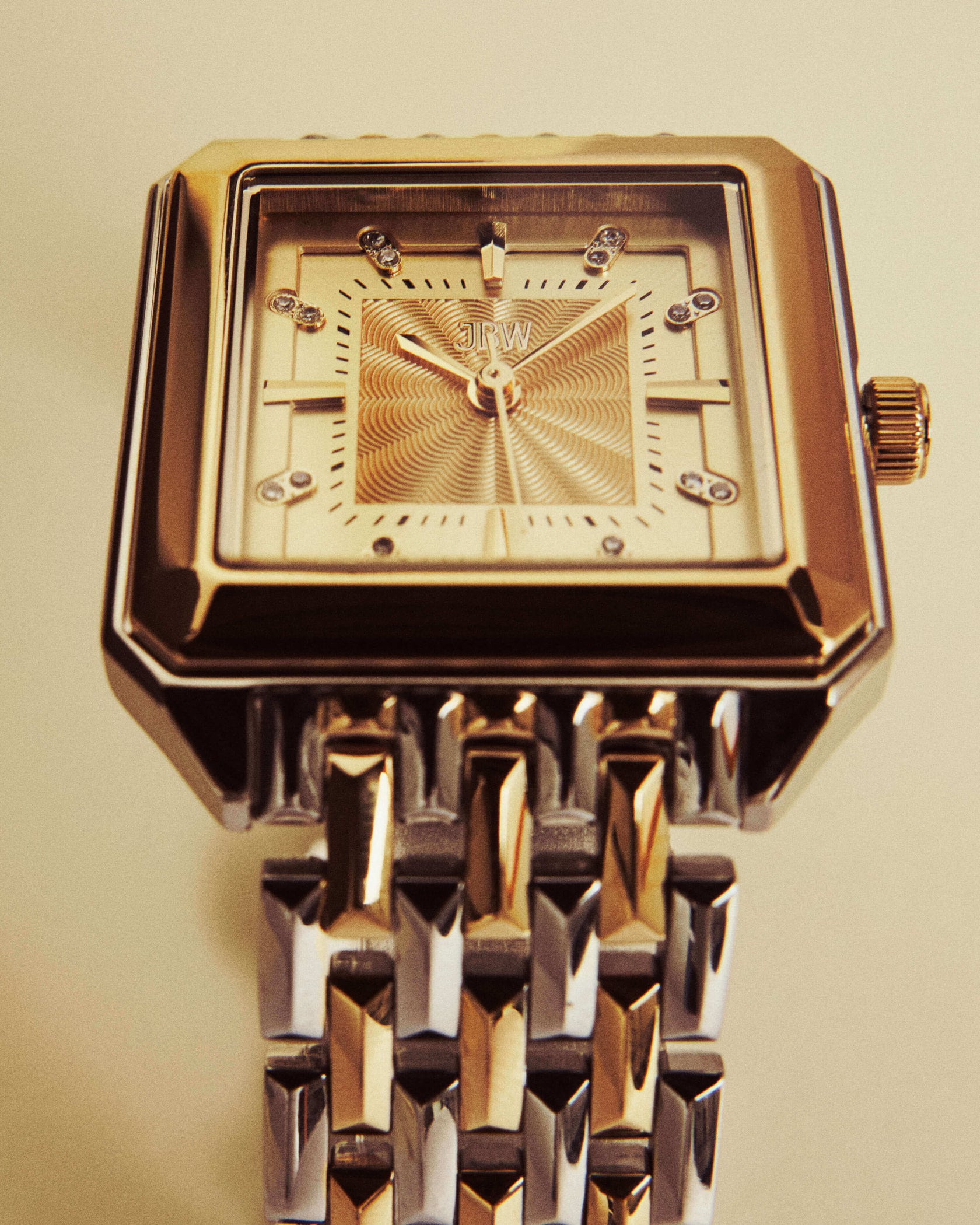 A close-up of the Astra | J6410C by JBW Watches, a gold and silver square-faced wristwatch featuring a stainless steel bracelet and decorative dial with the brand’s name on display.