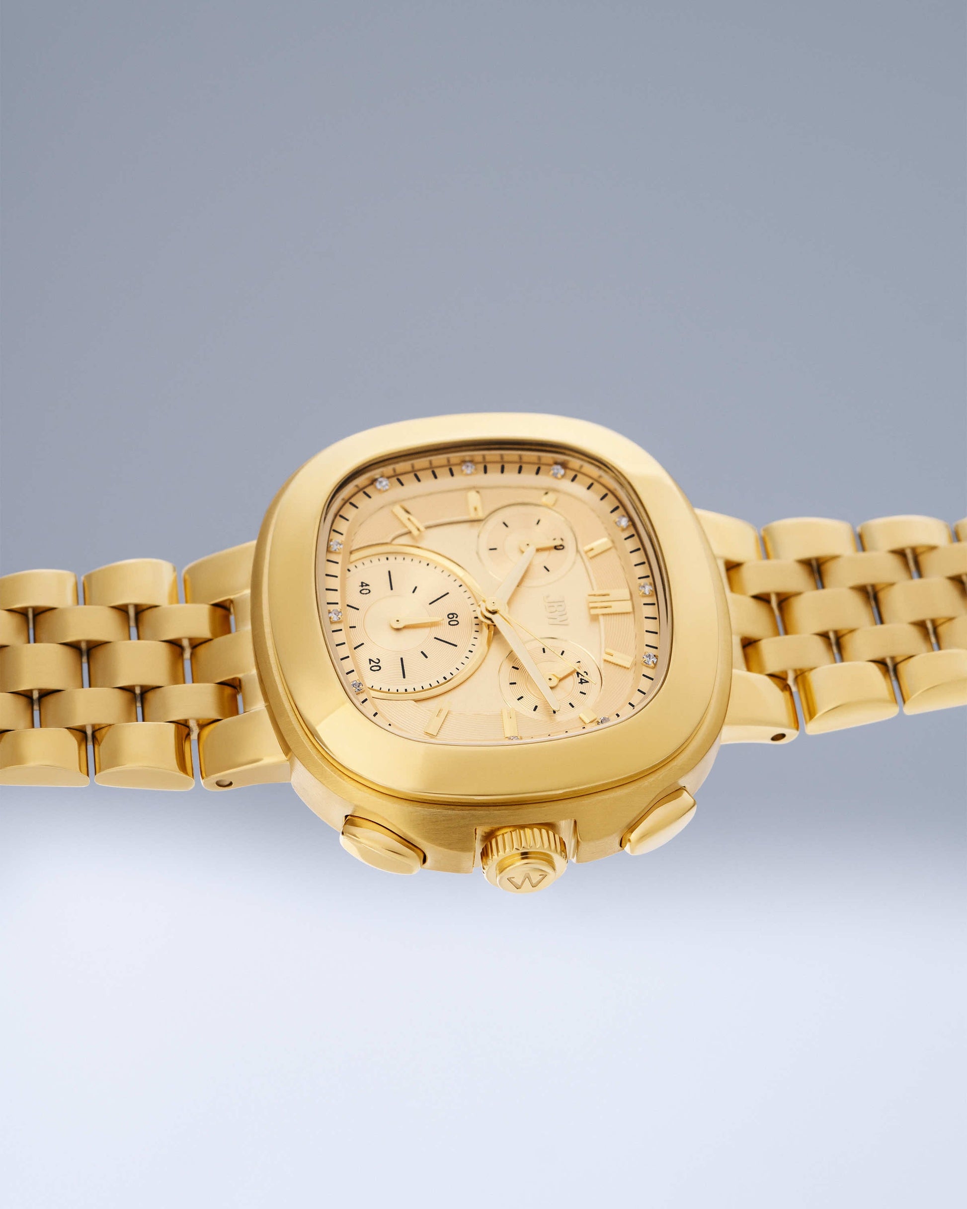 The JBW Watches Coast | J6397A is a gold chronograph with a square face, gold link bracelet, three subdials, and two side push buttons, displayed on a light gray gradient background.