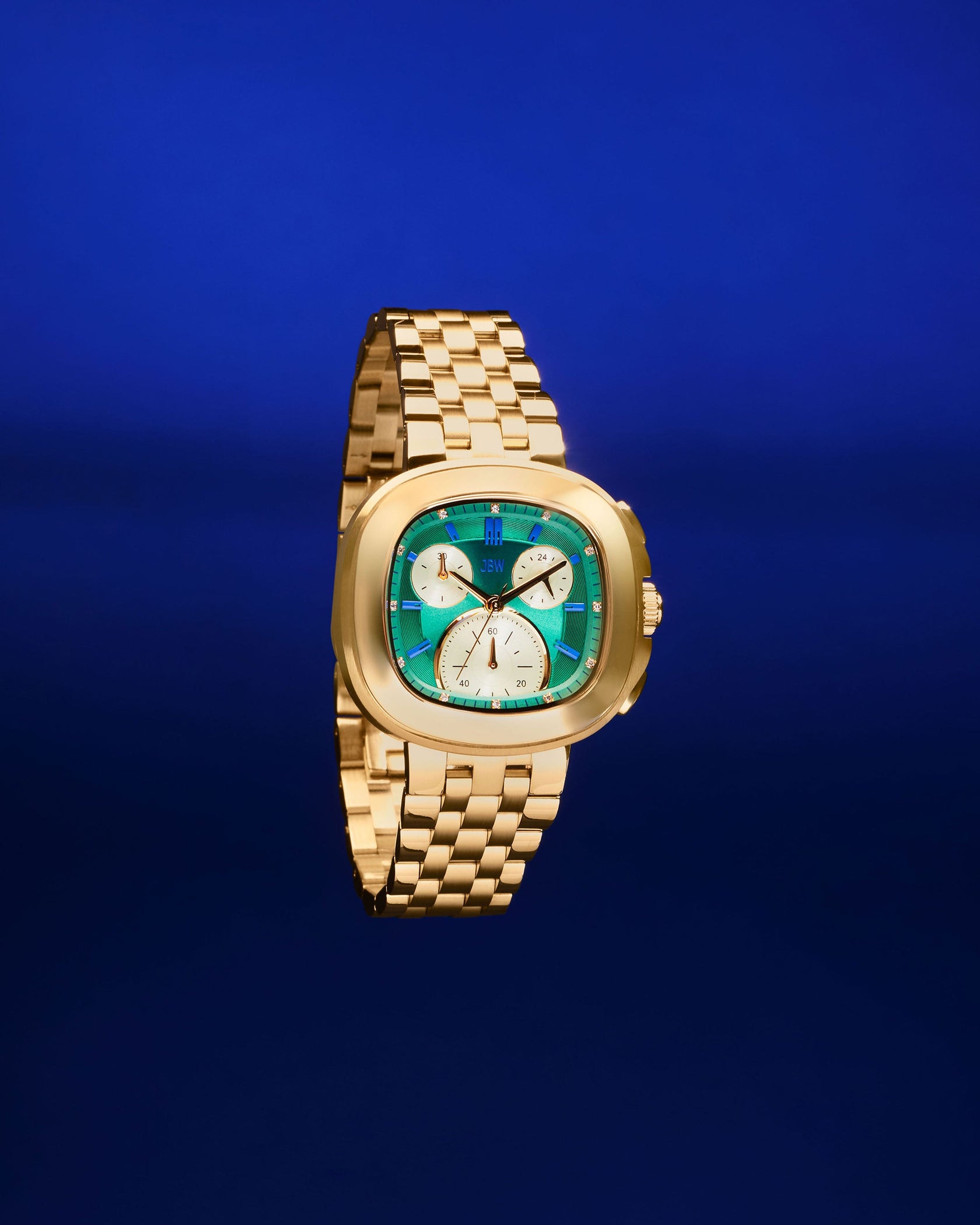 The JBW Watches Coast | J6397D features a 38mm stainless steel case, gold link band, square turquoise face with three white subdials, and Japanese Miyota movement, shown against a solid blue background.