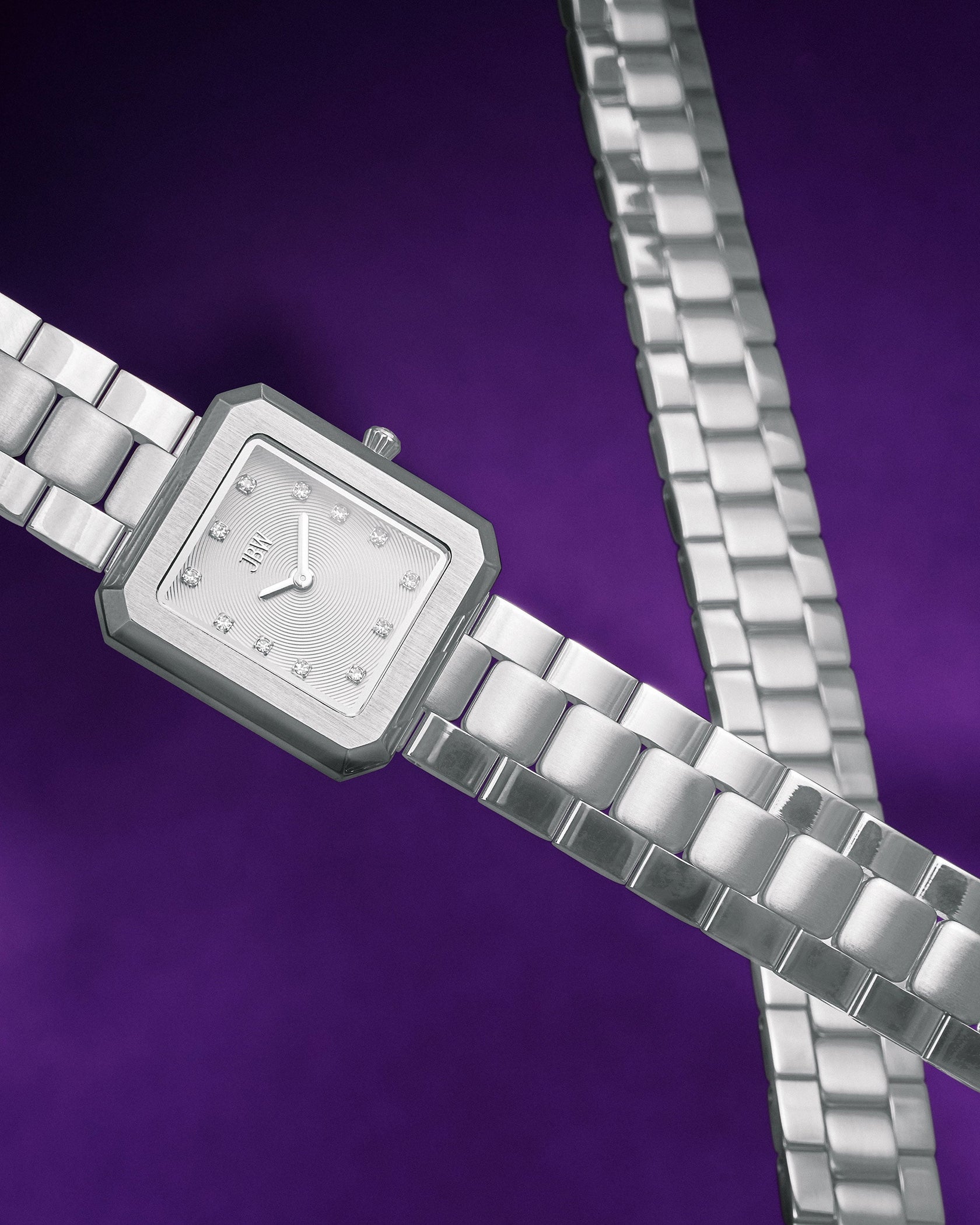 The JBW Watches Arc Double | J6390J, a silver square wristwatch with a metal link band, is displayed against a vibrant purple background. Its face features silver hands, small square hour markers, and a simple, elegant design.