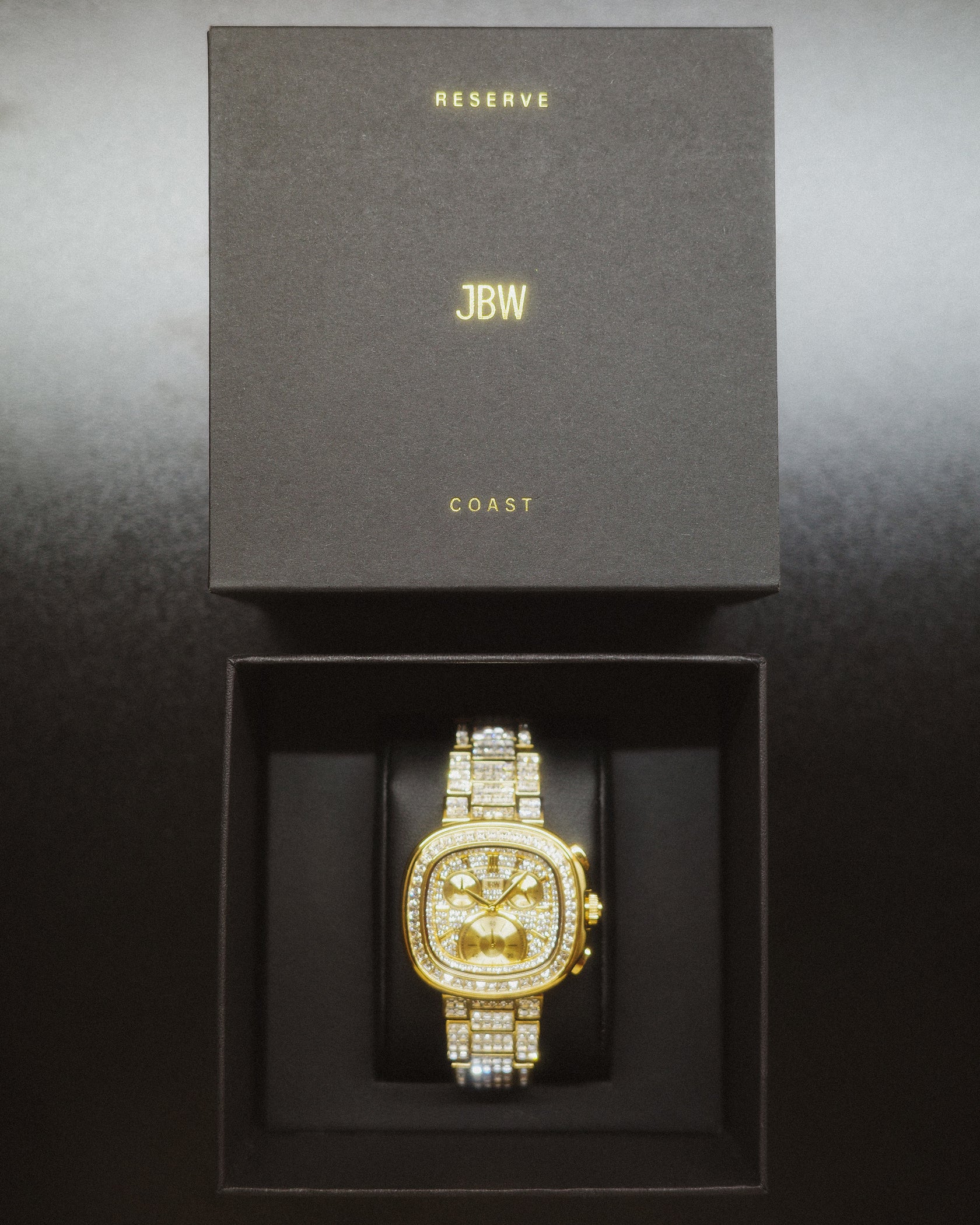 The RESERVE Coast Chandelier | R6397D by JBW Watches, a gold-tone chronograph with lab-grown diamonds, is showcased in an open black box featuring "RESERVE" and "COAST" above and below the JBW brand name on the lid.