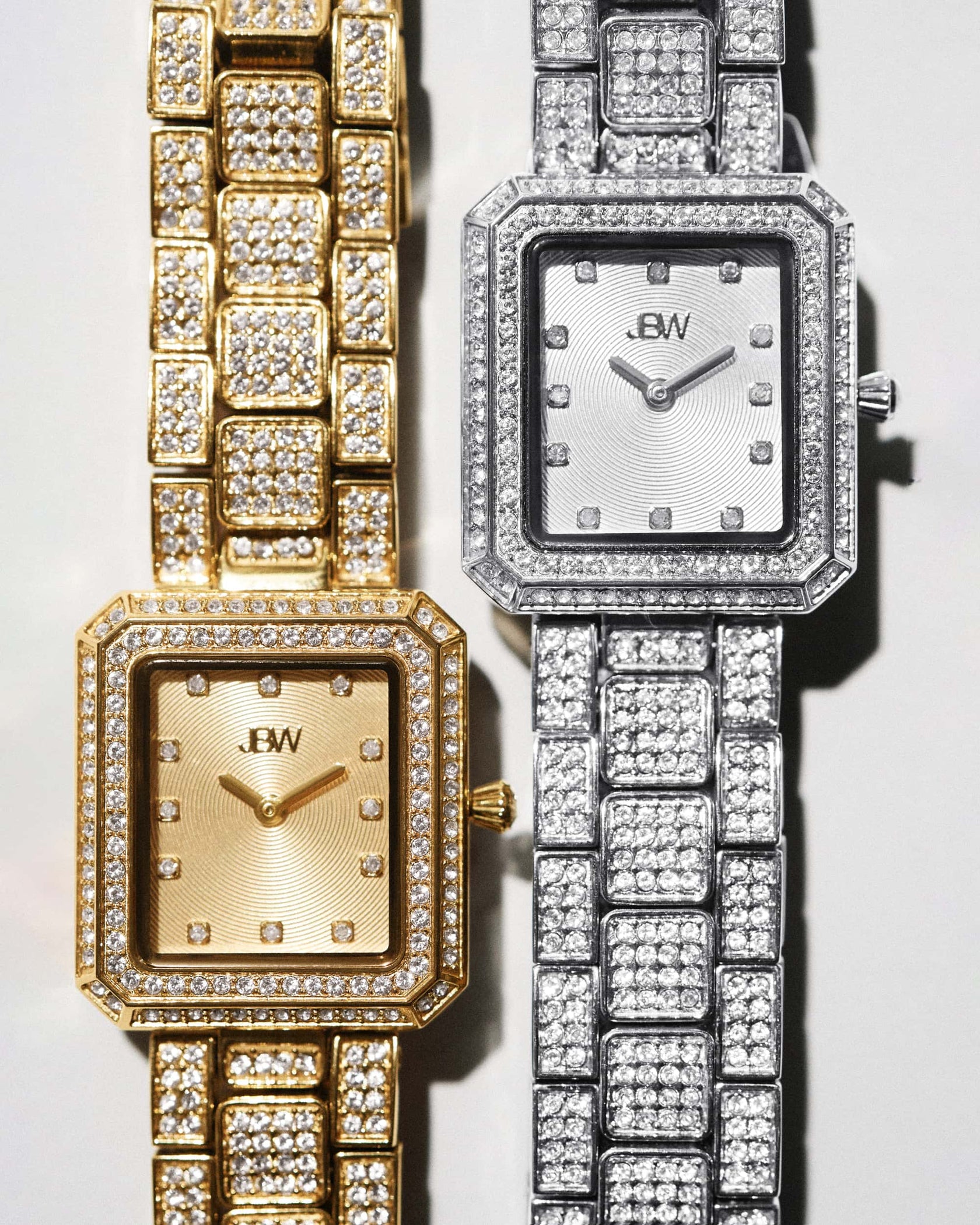 Two Arc Single | J6390B luxury wristwatches by JBW Watches—one gold, one silver—with rectangular faces and crystal-studded bezels are displayed side by side on a light background.
