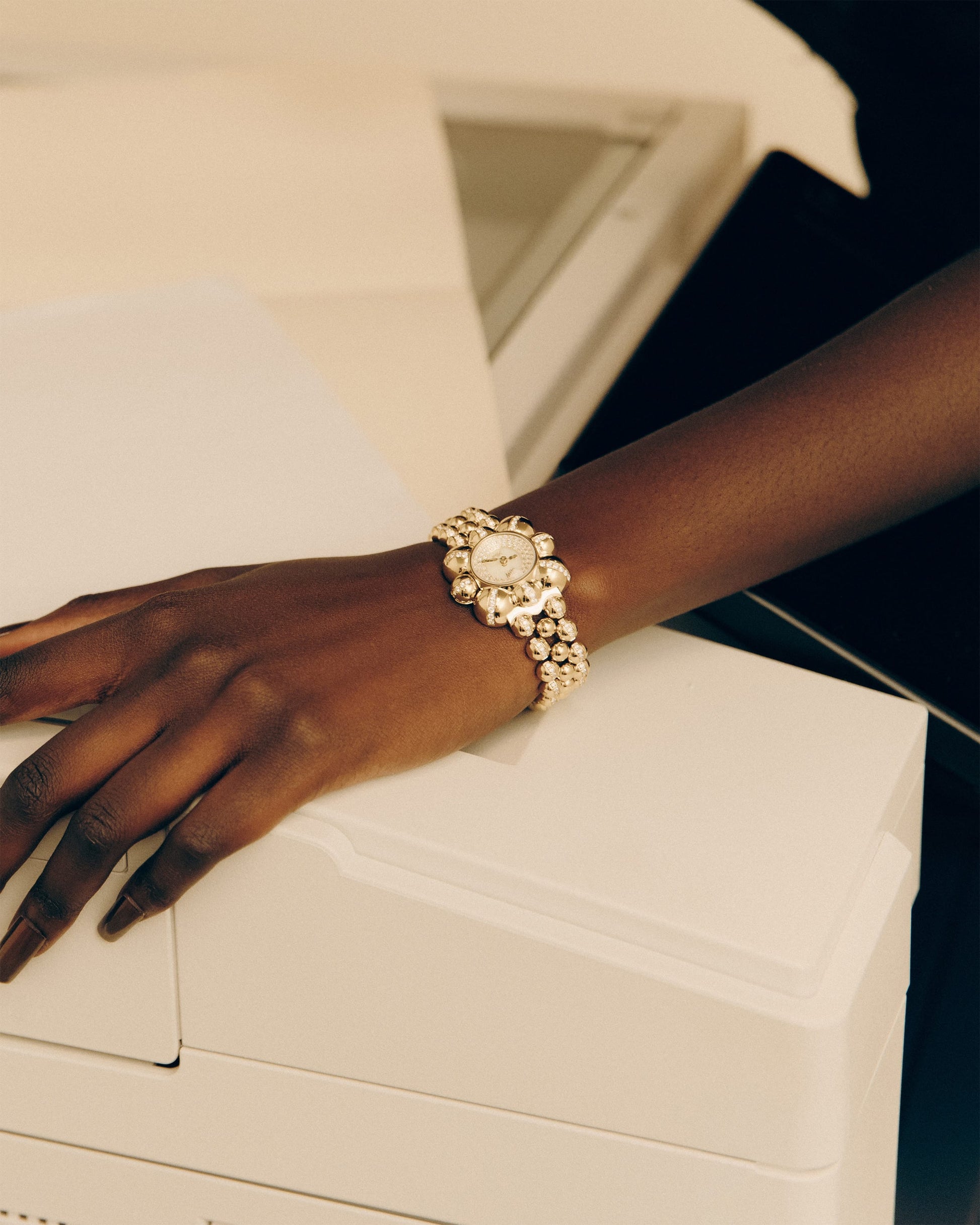 A close-up of a hand on a white machine, wearing the JBW x Luar – Atmosphere (Sample Sale) | J6406A-SC by JBW Watches, an 18k gold-plated watch with pearl-like beads, reminiscent of limited edition jewelry.