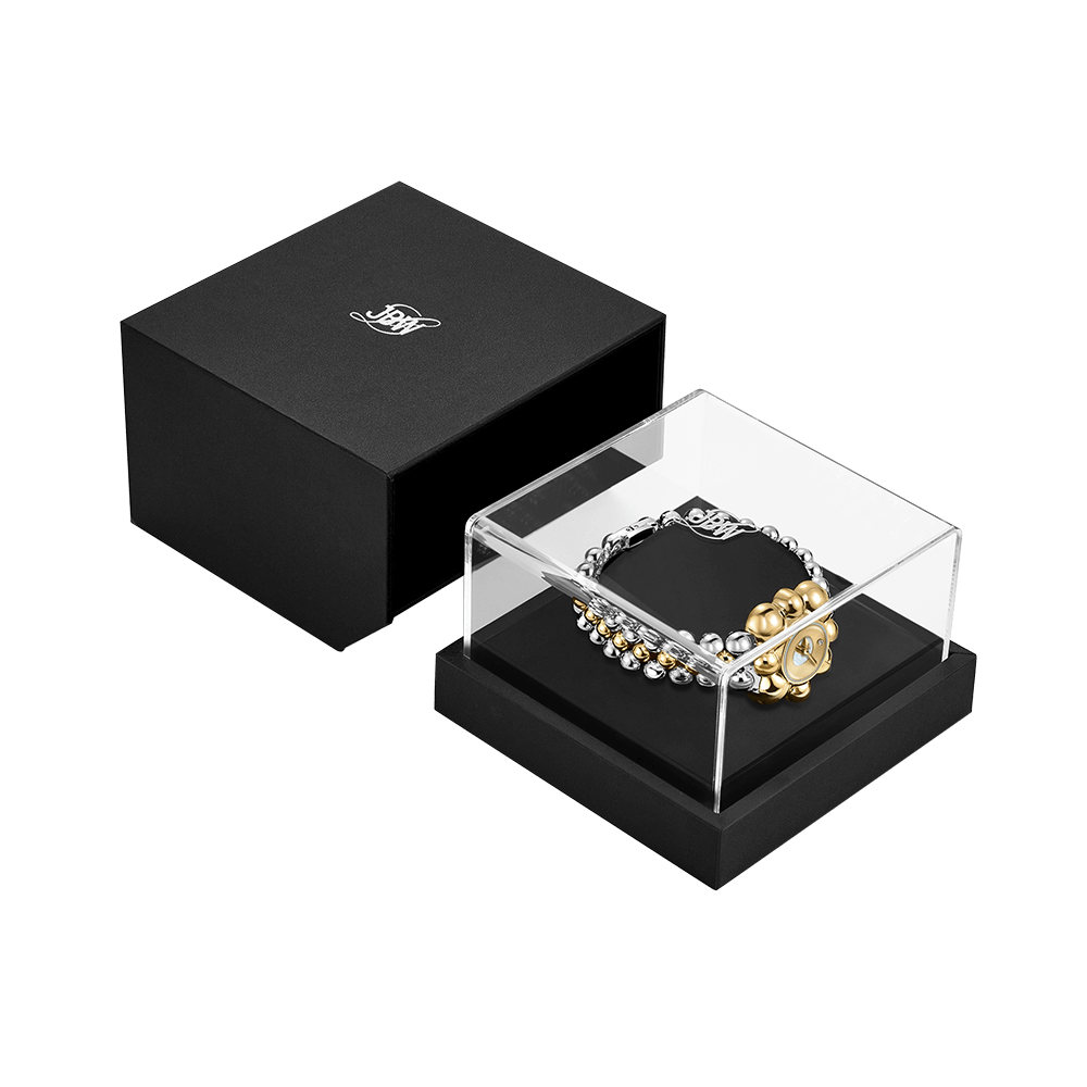 A black JBW Watches gift box with a logo sits next to a clear case displaying three limited-edition JBW x Luar – Atmosphere (Sample Sale) metallic beaded bracelets in silver and gold, neatly arranged inside.