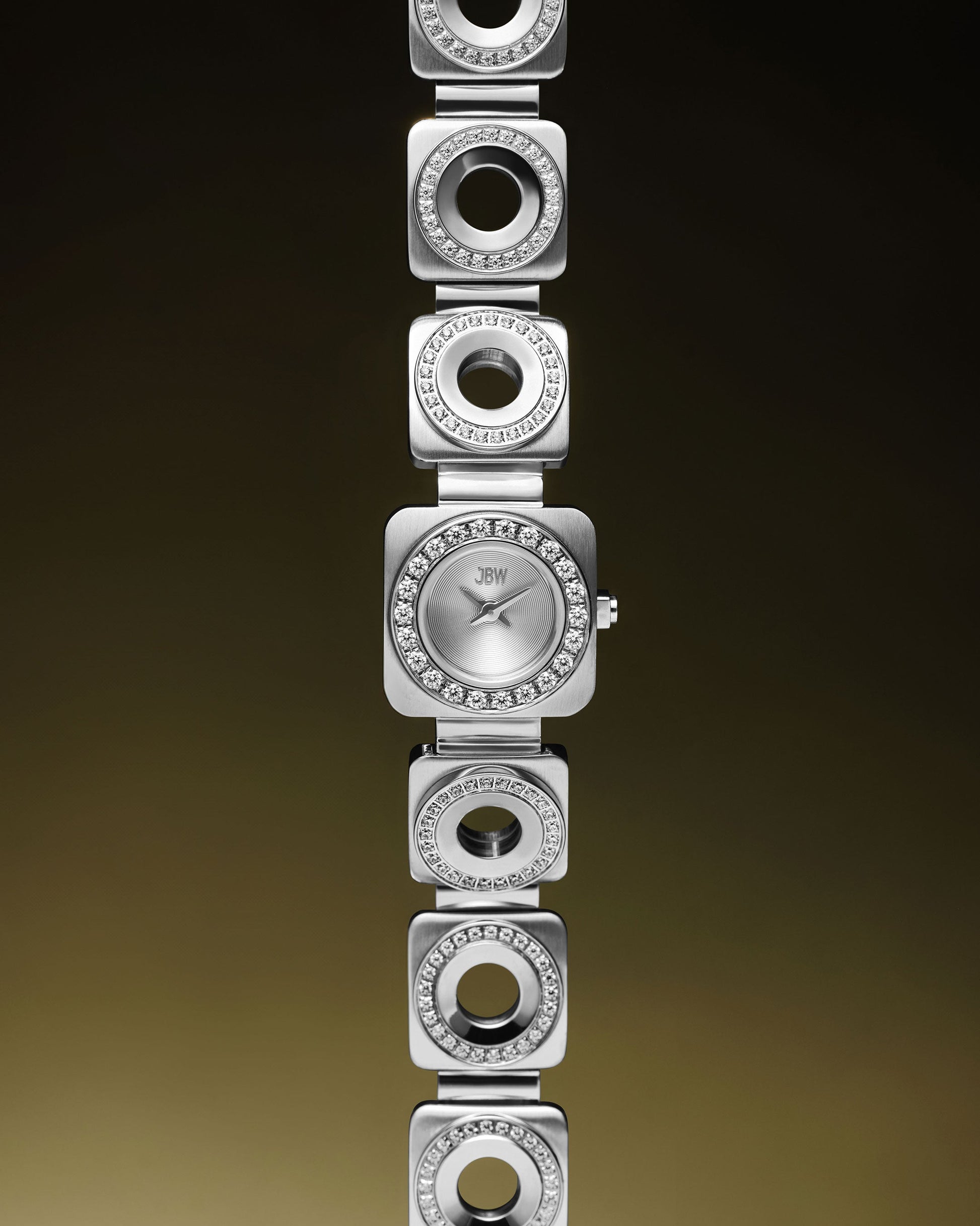 The Chasm Petite (Sample Sale) | J6401B-GA by JBW Watches is a silver stainless steel watch with a square face, premium crystal accents, and a unique bracelet of alternating solid/open links, shown against a gradient brown background.