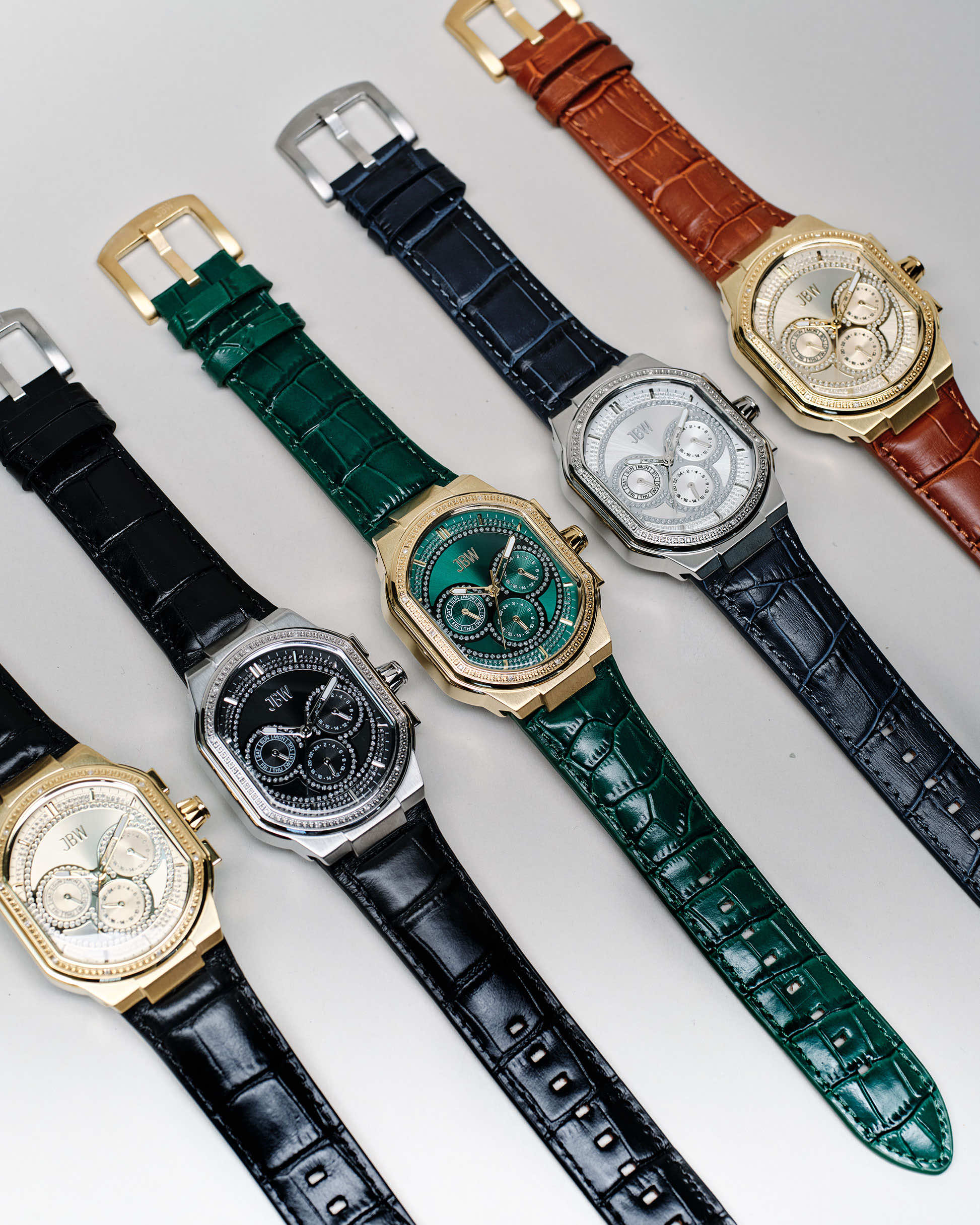 Five JBW Orion | J6408E luxury watches with textured dials and black, green, or brown leather straps are displayed diagonally. Each features a gold or silver case, detailed chronograph face, and precision Japan-made movement.