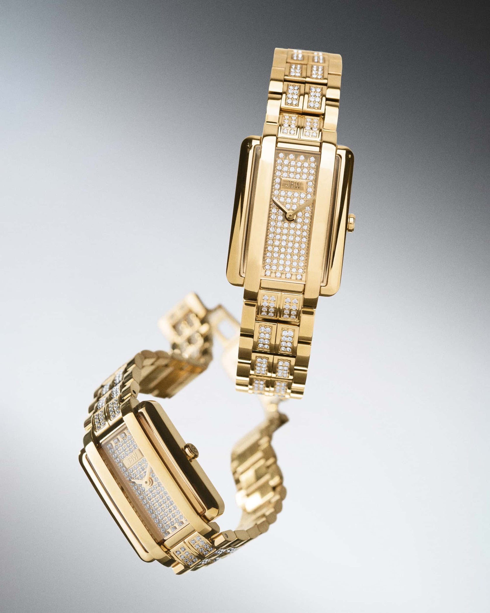 Two gold Mink Petite | J6394A luxury wristwatches by JBW Watches, featuring rectangular faces and lab grown diamond-studded bands and dials, are displayed on a gradient gray background to highlight their shine and elegance.