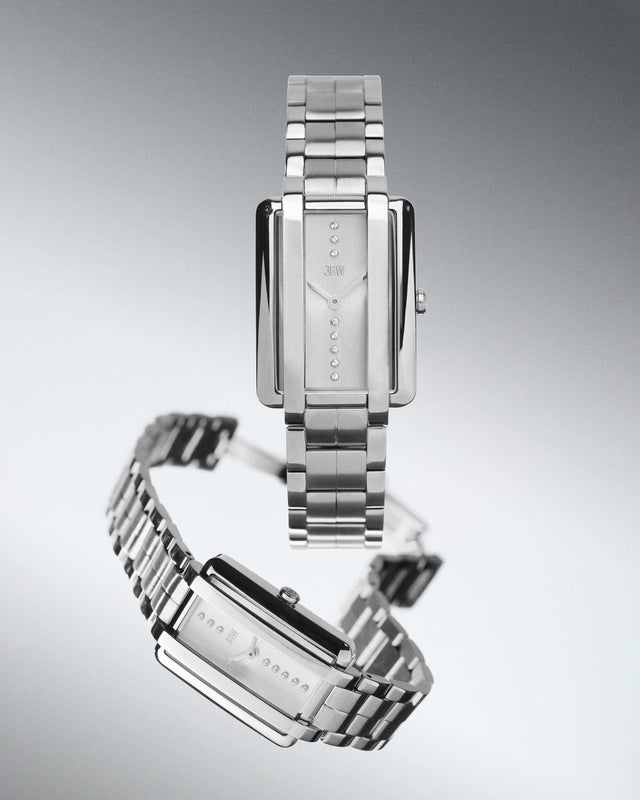 The JBW Watches Mink Petite | J6395B is a silver rectangular luxury watch featuring a metal link band, minimalist face, and twelve lab grown diamonds in a vertical line. It has simple hands, no numerals, and the JBW logo below the diamonds.